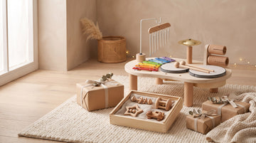 Wooden musical activity table and a box of beech baby rattles beside kraft-wrapped gifts with linen ribbon
