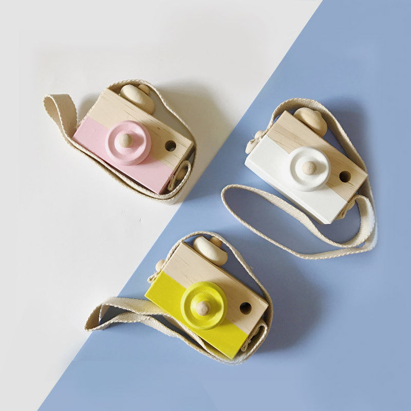 Pink, white and yellow wooden toy cameras on a two-tone background