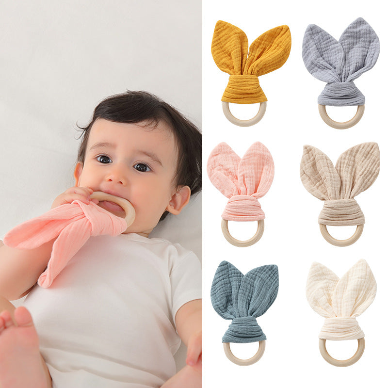 Baby holding a muslin bunny ear teether ring with colour options