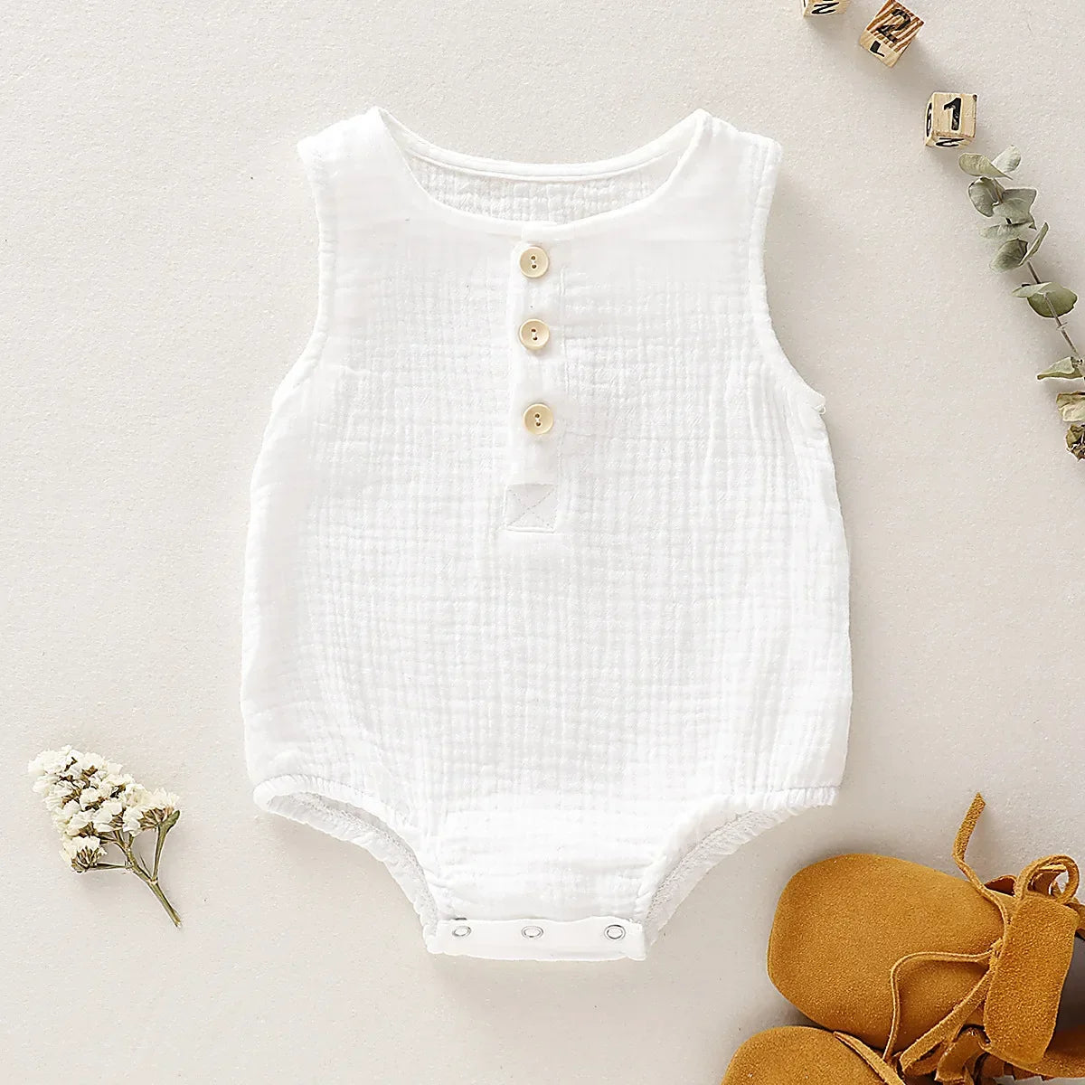 the BabyLove Sleeveless Romper at BubeBaby, designed for babies 0-24 months. Made from soft cotton, this solid-colored romper features an O-neck and covered button closure, perfect for summer