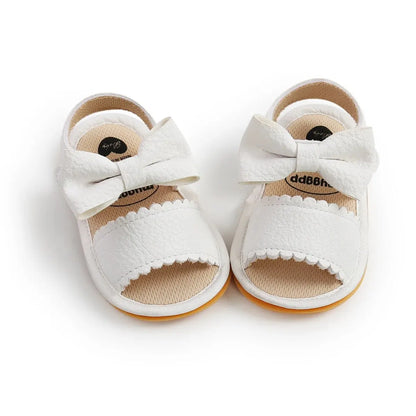 A cute pair of Bubebaby BabyLove  faux leather sandals for infants featuring an adorable bow detail. The sandals are designed for comfort and style, perfect for little ones to wear during warm weather. The adjustable strap ensures a secure fit while the soft sole provides cushioning for tiny feet