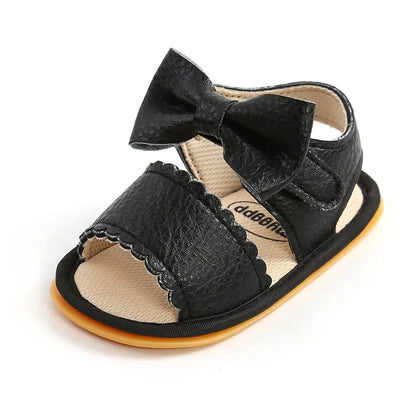 A cute pair of Bubebaby BabyLove  faux leather sandals for infants featuring an adorable bow detail. The sandals are designed for comfort and style, perfect for little ones to wear during warm weather. The adjustable strap ensures a secure fit while the soft sole provides cushioning for tiny feet