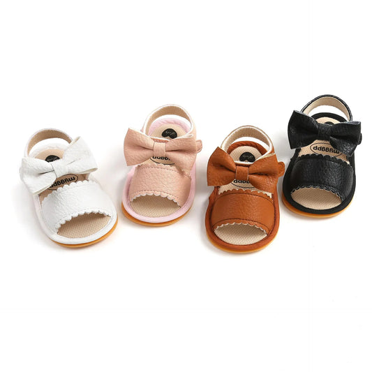 A cute pair of Bubebaby BabyLove  faux leather sandals for infants featuring an adorable bow detail. The sandals are designed for comfort and style, perfect for little ones to wear during warm weather. The adjustable strap ensures a secure fit while the soft sole provides cushioning for tiny feet