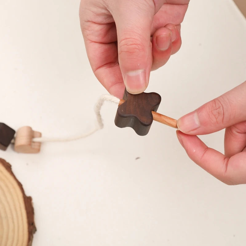 Hands threading a dark walnut star onto the cotton cord