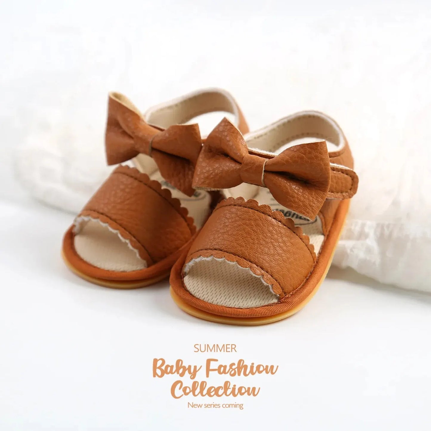 A cute pair of Bubebaby BabyLove  faux leather sandals for infants featuring an adorable bow detail. The sandals are designed for comfort and style, perfect for little ones to wear during warm weather. The adjustable strap ensures a secure fit while the soft sole provides cushioning for tiny feet